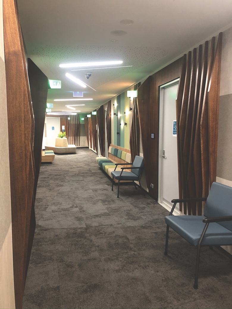 View down a brightly-lit wide hallway at TASCAT, with mid-grey carpet and a row of chairs against the wall.