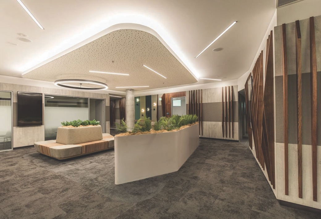 The reception area at TASCAT, a large room with mid-grey carpet and beige walls and ceiling. The walls are lined with vertical timber decoration. There are two raised beds of plants in the middle of the room